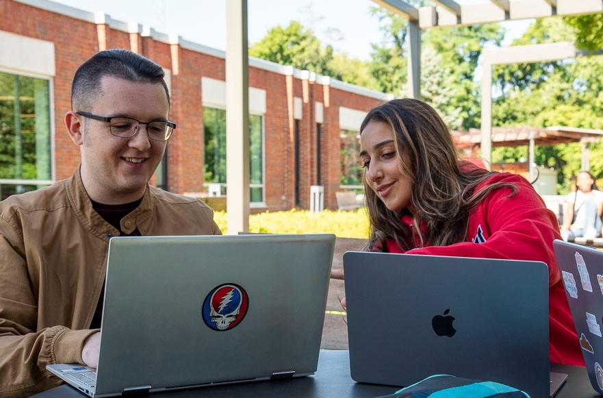 two students sitting outside at a table with a laptop