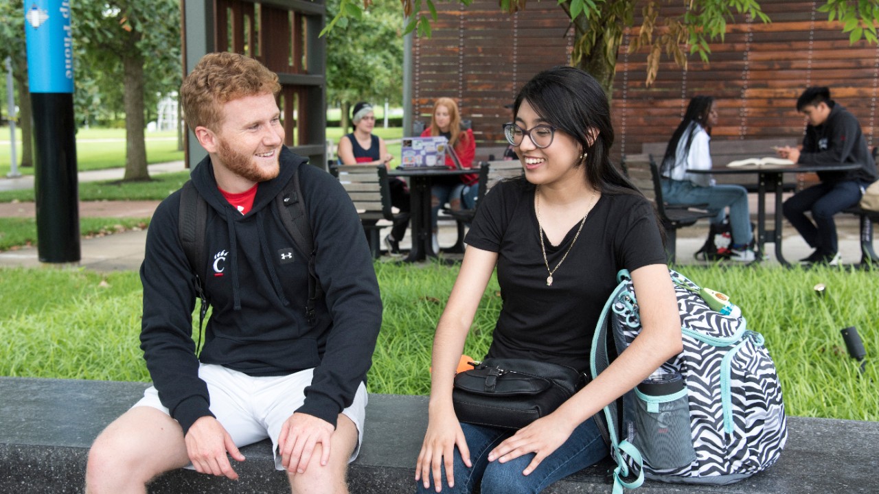 Two students smiling and talking outside on the UC Blue Ash patio