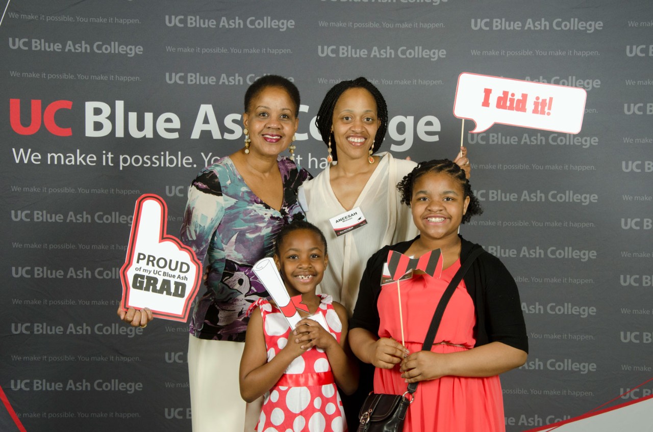 New graduate posing with her family in front of college backdrop